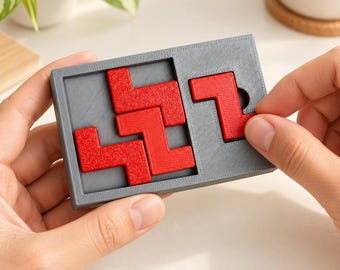 Può includere: Una cornice rettangolare grigia per puzzle contenente quattro pezzi geometrici rossi a incastro. La cornice ha una superficie ruvida con un'area incassata dove sono disposte le forme rosse. Un pezzo rosso viene spostato all'interno della cornice.