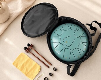 May include: A teal steel tongue drum with gold-colored numbers sits inside a black circular carrying case. Included are two wooden mallets with black tips, a yellow cleaning cloth, four black finger picks, and a sticker sheet with numbers 1-7.