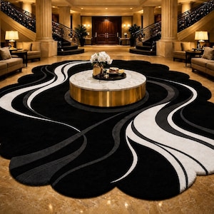May include: A large, circular area rug featuring a scalloped edge and a flowing, abstract pattern in black, white, and gray. The rug is positioned beneath a round coffee table with a white marble top and a cylindrical gold metal base.