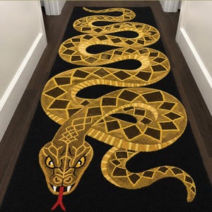 Puede incluir: Una alfombra pasillera rectangular larga con fondo negro y un diseño de serpiente grande y sinuosa en tonos amarillo, dorado y marrón. La serpiente tiene una cabeza detallada con ojos amarillos, colmillos blancos y una lengua bífida roja.