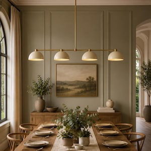 May include: A linear chandelier featuring a long, thin brass rod suspended from the ceiling, supporting four evenly spaced, dome-shaped off-white metal shades that direct light downward over a long wooden dining table.