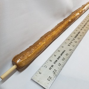 May include: A long, natural wood walking stick with a smooth, polished finish. The stick is approximately 20 inches long and has a natural wood color. The stick is measured against a ruler.
