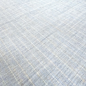 May include: Close-up of a light blue woven fabric with a subtle grid pattern. The fabric has a textured appearance, with visible threads creating a slightly uneven surface. The color is a soft, muted blue.