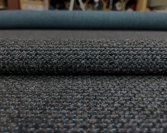 May include: A roll of dark charcoal gray fabric featuring a textured, nubby weave with small, evenly spaced light blue thread accents throughout. The material has a thick, heavy appearance with a consistent grid-like pattern across the surface.