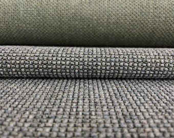 May include: A close-up view of two stacked layers of heavy-duty upholstery fabric. The top layer is a solid olive green with a fine, tight weave. The bottom layer is a textured, multi-tonal gray fabric featuring a prominent, raised grid pattern.