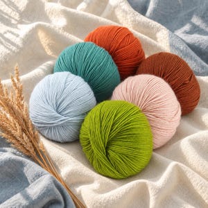 May include: A collection of six round yarn balls in vibrant colors including orange, teal, light blue, lime green, soft pink, and brown, arranged together with a bundle of dried wheat stalks, showcasing the textured, twisted fiber construction.
