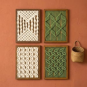 May include: Four rectangular wall art pieces featuring intricate macrame cord designs in cream and sage green, each encased in a dark wooden frame. Two frames display cream-coloured cord patterns, while two display green cord patterns. A small woven basket hangs nearby.