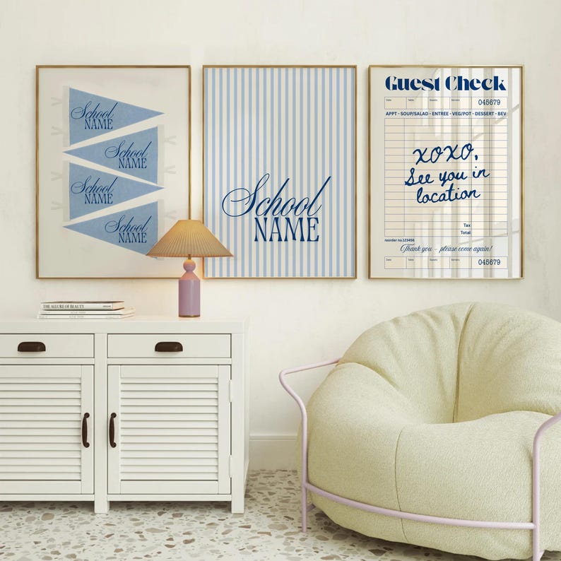 May include: Three framed wall art prints displayed above a white cabinet with a lamp. The left print shows blue pennants with the text School Name. The center print features blue vertical stripes and the text School Name. The right print is a guest check.