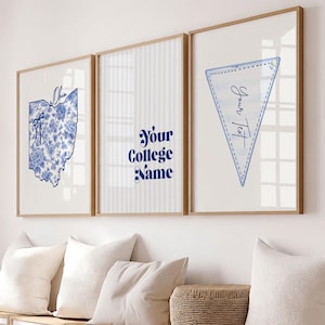 May include: Three framed wall art prints with light wood frames. The left print shows a blue floral Ohio state map with the text Ohio. The center print features vertical stripes and the text Your College Name. The right print shows a blue pennant with the text Your Text.