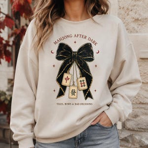 Woman wearing an oversized cream sweatshirt with a black bow and Mahjong tile game night design.