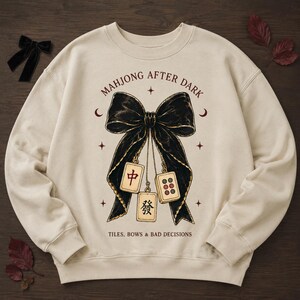 Cream sweatshirt flat lay featuring the Mahjong After Dark bow PNG on a dark wood background.
