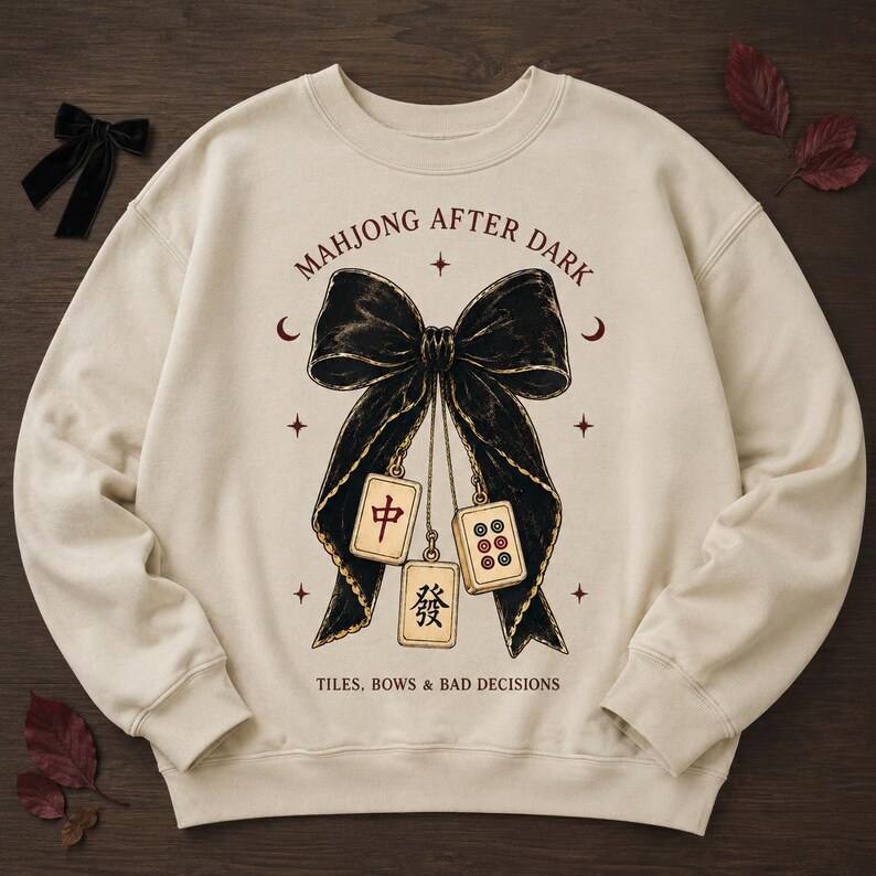 Cream sweatshirt flat lay featuring the Mahjong After Dark bow PNG on a dark wood background.