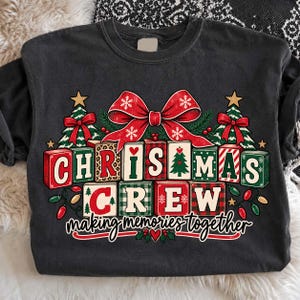 May include: A charcoal gray crewneck t-shirt featuring a graphic of alphabet blocks spelling CHRISTMAS CREW with the text making memories together. The design includes a large red bow, two Christmas trees, and colorful holiday light bulbs.