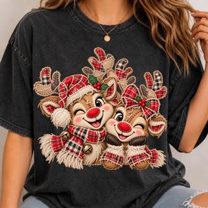Può includere: Una t-shirt grigio antracite a maniche corte con una grafica di due renne cartoon con texture effetto cucitura. Le renne indossano sciarpe, cappelli e fiocchi a quadri rossi e neri, con piccoli campanellini dorati e decorazioni di agrifoglio.