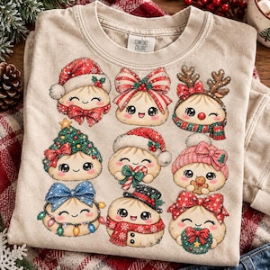 May include: A beige crewneck t-shirt featuring a graphic print of nine cartoon dumplings with various Christmas-themed accessories, including Santa hats, reindeer antlers, bows, scarves, and holiday lights, with a Comfort Colors brand label.