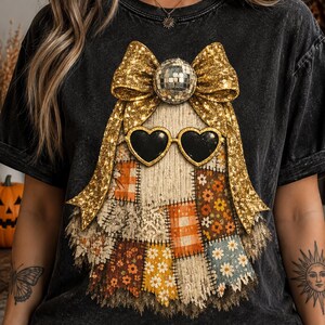 Peut inclure: Un t-shirt noir délavé à l'acide avec un motif central représentant un fantôme composé de divers patchs en tissu à motifs. Le fantôme porte des lunettes de soleil en forme de cœur noir et est surmonté d'un grand nœud doré pailleté et d'une boule à facettes.