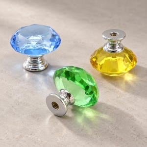 May include: Three faceted cabinet knobs with a circular, diamond-like shape. One knob is light blue, one is bright yellow, and one is vibrant green. Each knob features a polished silver-tone metal base with a threaded hole for mounting hardware.