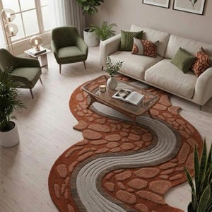 May include: An area rug with an irregular, organic shape featuring a textured, raised pattern of terracotta-colored stones and a central, winding river-like path in shades of light gray and brown, laid out on a light-colored wooden floor.