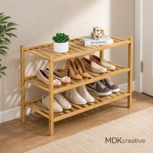 May include: A three-tier bamboo shoe rack with a slatted design. The top shelf holds a small green succulent in a white ribbed pot and a white book with wooden alphabet blocks. Various styles of shoes are arranged on the middle and bottom shelves.