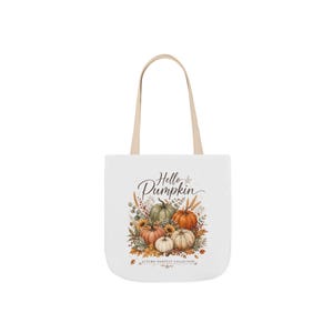 May include: A white tote bag with two beige handles featuring a graphic of various pumpkins, wheat, and autumn leaves. The text "Hello Pumpkin" is printed in a dark script font above the pumpkins, with "AUTUMN HARVEST COLLECTION" below.