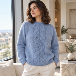 Könnte beinhalten: Ein hellblauer, langärmeliger Strickpullover mit einem vertikalen Mittelstreifen aus einem komplexen Zopf- und Lochmuster, einem Rundhalsausschnitt sowie gerippten Bündchen an Ärmeln und Saum, kombiniert mit einer cremeweißen Hose.