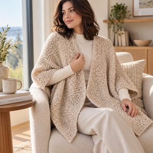 May include: A beige open-front cardigan featuring a chunky, textured knit pattern with wide sleeves. The garment is worn over a solid cream-colored long-sleeve top and matching cream-colored trousers, creating a layered, neutral-toned ensemble.