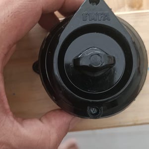 May include: A round black electrical rotary switch featuring a central knob and a triangular mounting flange at the top. The word EMFA is embossed in capital letters on the upper portion of the black plastic housing, which includes two screw holes.