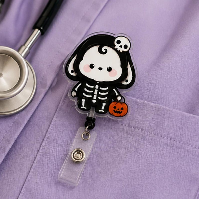May include: A retractable badge reel featuring a cartoon character dressed in a black skeleton costume with a white skull on its head. The character has pink cheeks and holds a small orange jack-o'-lantern. The reel is attached to a clear plastic strap.