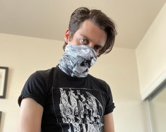 May include: A person wearing a black t-shirt with a graphic print of a creature with wings. The person is wearing a grey and white patterned face mask.