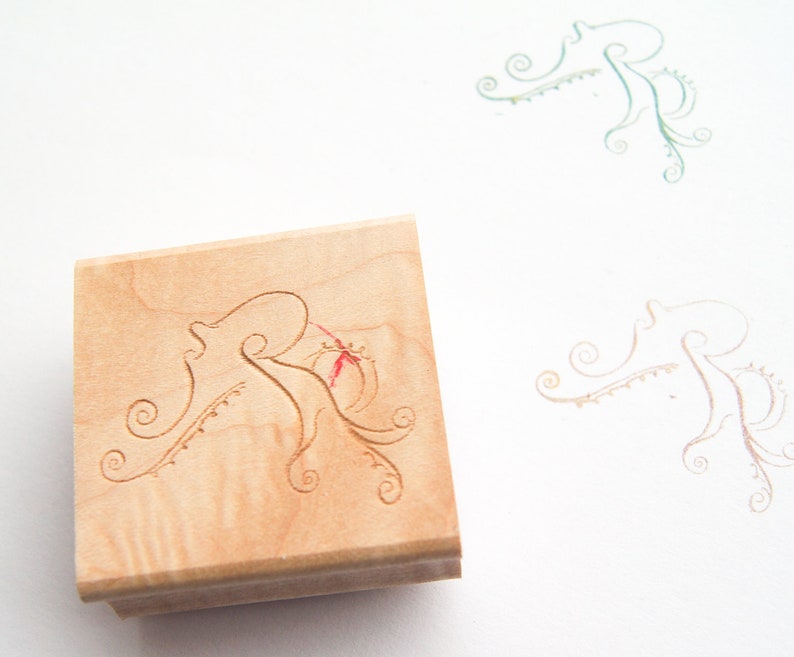 May include: A wooden stamp with a carved design of an octopus with intricate details. The stamp is light brown with a natural wood grain.