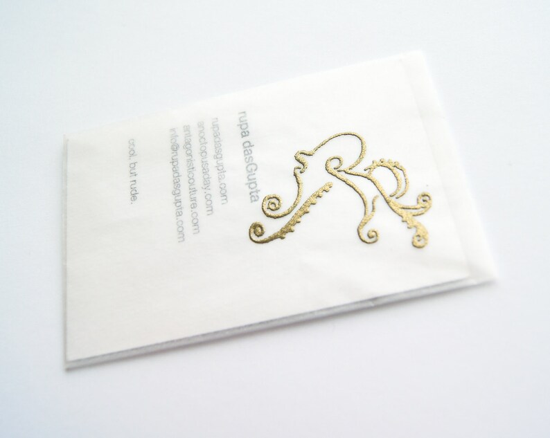 May include: White business card with gold lettering. The text reads "rupa dasGupta" and includes the website address "rupadasgupta.com". A stylized gold octopus design is in the upper right corner.