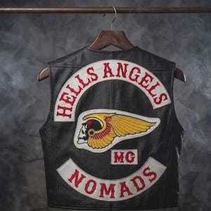 Könnte beinhalten: Eine schwarze Lederweste mit einem großen gestickten Aufnäher auf der Rückseite. Der Aufnäher zeigt den Text HELLS ANGELS in Rot auf einem weißen Bogen, ein geflügeltes Totenkopf-Emblem in Gelb und Rot, die Buchstaben MC und das Wort NOMADS in Rot.
