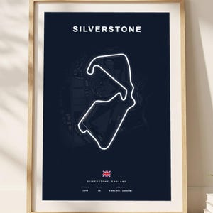 May include: A framed poster featuring a dark blue background with a white outline of the Silverstone race track. The text reads SILVERSTONE at the top, with the British flag, location, opening year 1948, 18 turns, and 5.891 KM / 3.660 MI length.