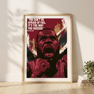 May include: A framed poster featuring a stylized graphic illustration of LeBron James with a dark red and black color palette. The text reads, 'YOU CAN'T BE AFRAID OF FAIL. IT'S THE WAY YOU SUCCEED.' with the name LeBron James printed below.