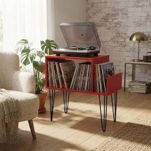 May include: A red wooden record player stand with black metal hairpin legs, featuring two open storage compartments filled with vinyl records and a turntable with a clear dust cover placed on the top surface of the unit.