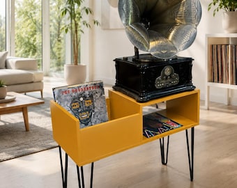 May include: A mustard yellow vinyl record storage console with black hairpin legs, featuring two open compartments holding vinyl records. A black vintage-style gramophone with a large metallic silver horn sits on top of the console.