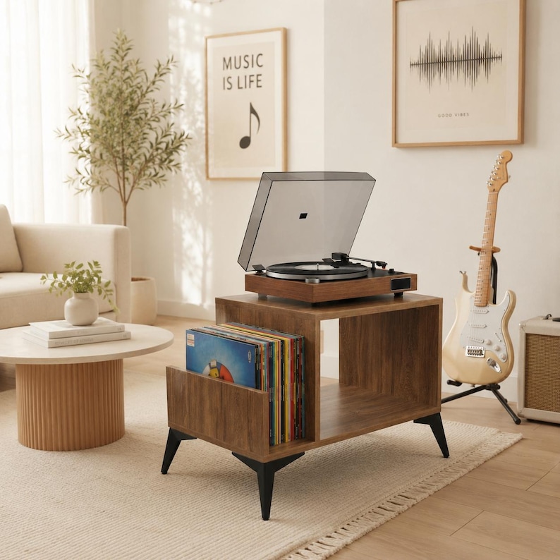 May include: A brown wooden record player stand with black metal legs, featuring an open storage compartment for vinyl records. A turntable with a clear dust cover sits on the top surface of the stand, which is positioned in a room.