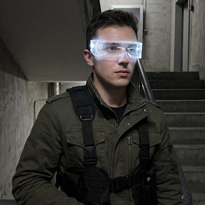 May include: A pair of futuristic LED visor glasses with a glowing white light display, worn over the eyes. The glasses feature a sleek, transparent frame with integrated circuitry patterns that illuminate brightly against the dark environment.