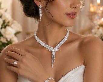 Könnte beinhalten: Ein silberfarbenes Schmuckset bestehend aus einer Halskette mit zentralem Blumenmotiv und herabhängenden Kristallfransen, passenden Ohrhängern mit einem Stein im Marquise-Schliff, einem zarten Kristallarmband und einem Ring mit Marquise-Stein.