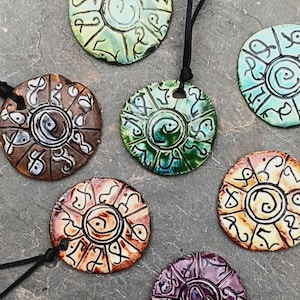 May include: Six round ceramic pendants with black cords. Each pendant features a different color glaze and a unique design of swirling lines and symbols.