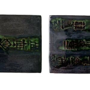 Peut inclure: Deux carreaux de céramique carrés avec un glaçage violet foncé et vert. Les carreaux présentent des motifs en relief texturés de couleur brun foncé. Les motifs ressemblent à de l'écriture ancienne.