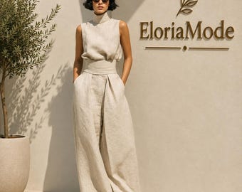 May include: A sleeveless beige jumpsuit with a high mock neck, a fitted waist, and wide-leg trousers. The garment features a textured fabric and is worn with black sunglasses and black sandals. The text EloriaMode is visible on the wall.