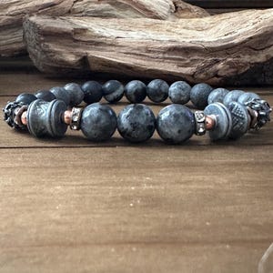 May include: A gray gemstone bracelet with silver and copper accents. The bracelet features round beads and decorative end caps.