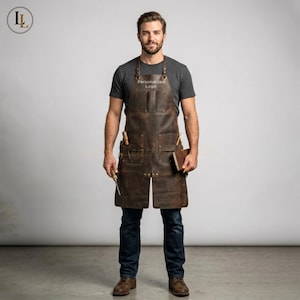 Könnte beinhalten: Eine dunkelbraune Lederschürze mit mehreren praktischen Taschen, verstellbaren Riemen mit Metallbeschlägen und einem Brustbereich mit dem Text Personalized Logo. Die Schürze wird über einem dunkelgrauen T-Shirt und einer dunkelblauen Jeans getragen.