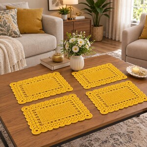 May include: A set of four rectangular mustard yellow placemats featuring a crocheted design with a solid center panel, a decorative openwork border, and a scalloped edge. The placemats are arranged on a wooden surface, showcasing the intricate texture.