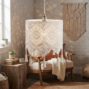May include: A cylindrical pendant lamp shade featuring an intricate white crochet pattern with a scalloped bottom edge. The shade is suspended by a cord and adorned with small wooden beads and hanging tassels along the lower perimeter.