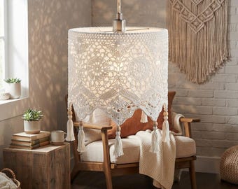 May include: A cylindrical pendant lamp shade featuring an intricate white crochet pattern with a scalloped bottom edge. The shade is suspended by a cord and adorned with small wooden beads and hanging tassels along the lower perimeter.