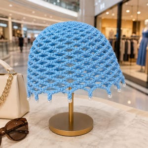 May include: A light blue crochet hat featuring an open diamond-shaped lattice pattern. The bottom edge of the hat is finished with a scalloped design, with each point accented by a small, round, white pearl bead attached to the crochet structure.
