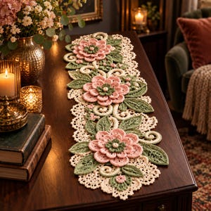 May include: A long, rectangular crochet table runner featuring three large, layered pink flowers with sage green centers, surrounded by intricate green crocheted leaves and cream-colored lace borders with swirling vine patterns.