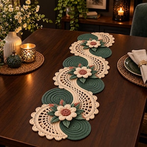 May include: A long, decorative table runner featuring a serpentine design of cream-colored crocheted lace and dark green circular woven mats. The runner is embellished with three-dimensional cream and pink floral motifs with green leaves.
